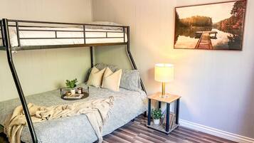 Ein Stockbett mit Nachttisch und Lampe, ein Gemälde eines Sees und ein Holzboden.