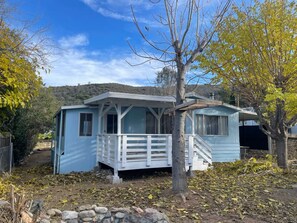 A small, single-story house with a porch and a covered area, surrounded by trees and a hilly landscape. - Charming Bodfish Home with Deck, Near Kern River (Bodfish)