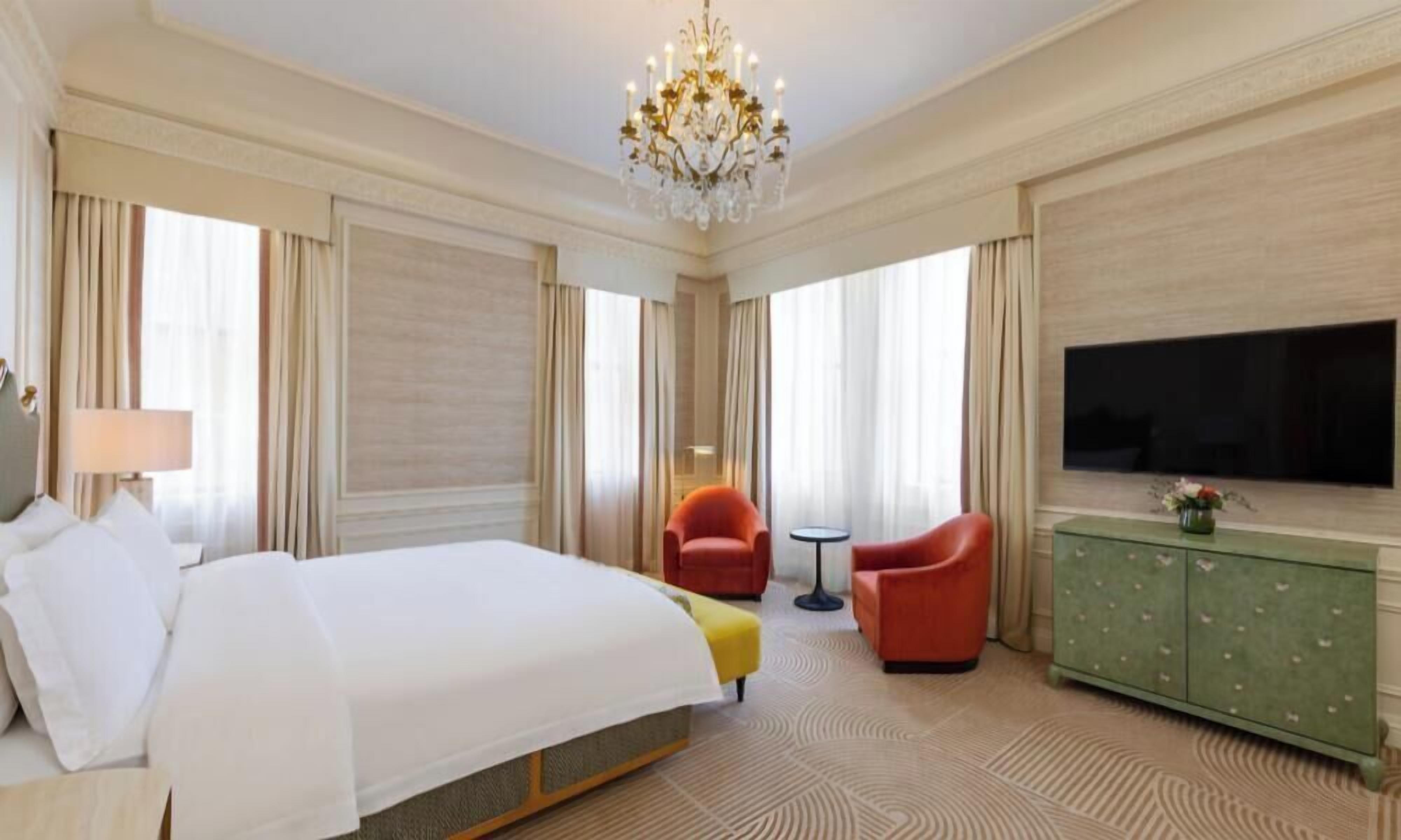 A hotel room with a large bed, a television, a green cabinet, and two red chairs.