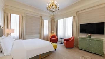 A hotel room with a large bed, a television, a green cabinet, and two red chairs.