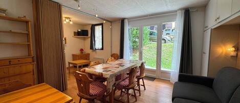 A dining area with a wooden table, chairs, and a television on a shelf.