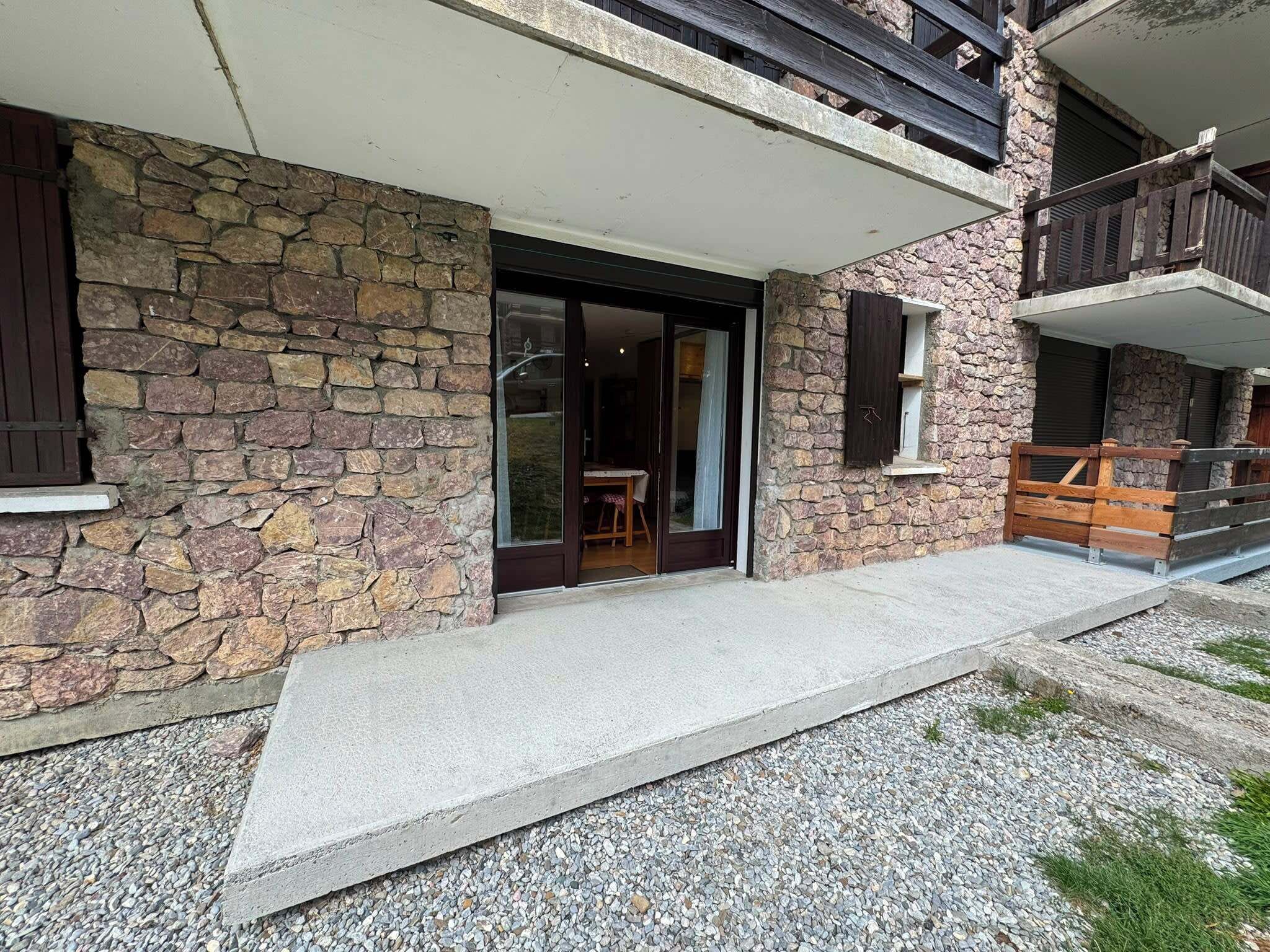 A stone facade with a glass door entrance, a concrete porch, and a wooden balcony.