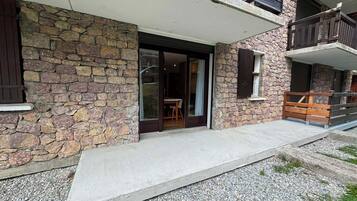 A stone facade with a glass door entrance, a concrete porch, and a wooden balcony.