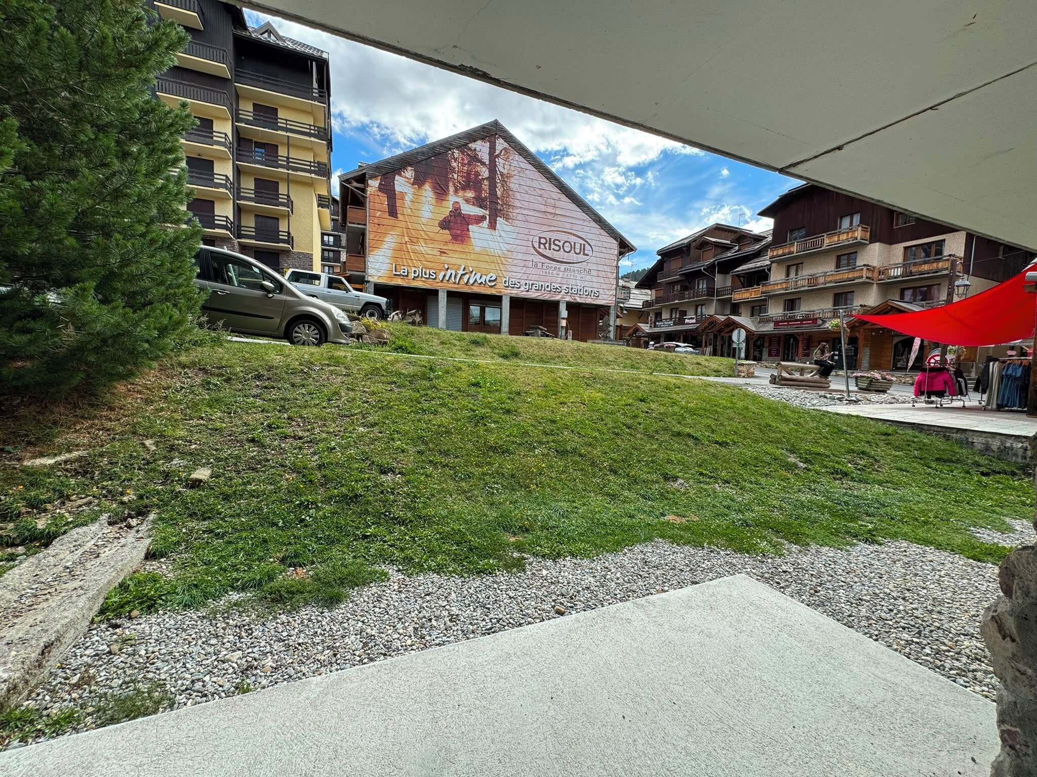A building with a large outdoor advertisement, a grassy area, and a parking lot with cars.