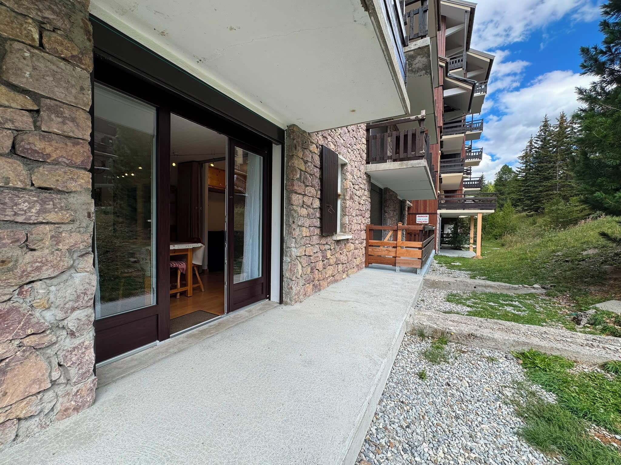 A modern building with a stone facade, large sliding glass doors, and a balcony with wooden railings.