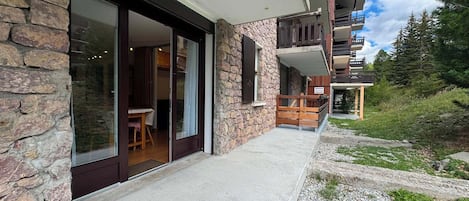A modern building with a stone facade, large sliding glass doors, and a balcony with wooden railings.