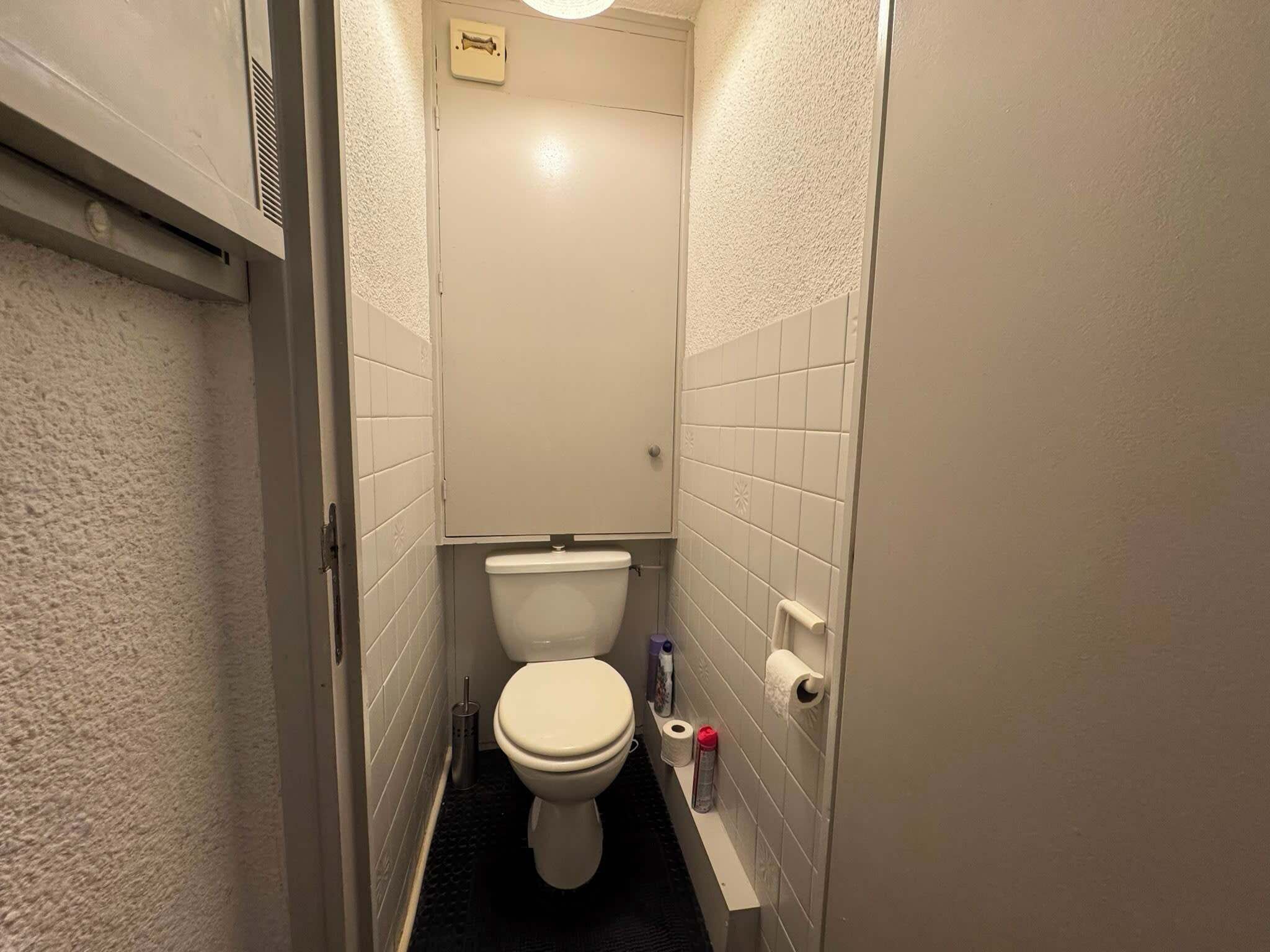 Un baño pequeño y estrecho con un inodoro, un secador de manos y un dispensador de toallas de papel.