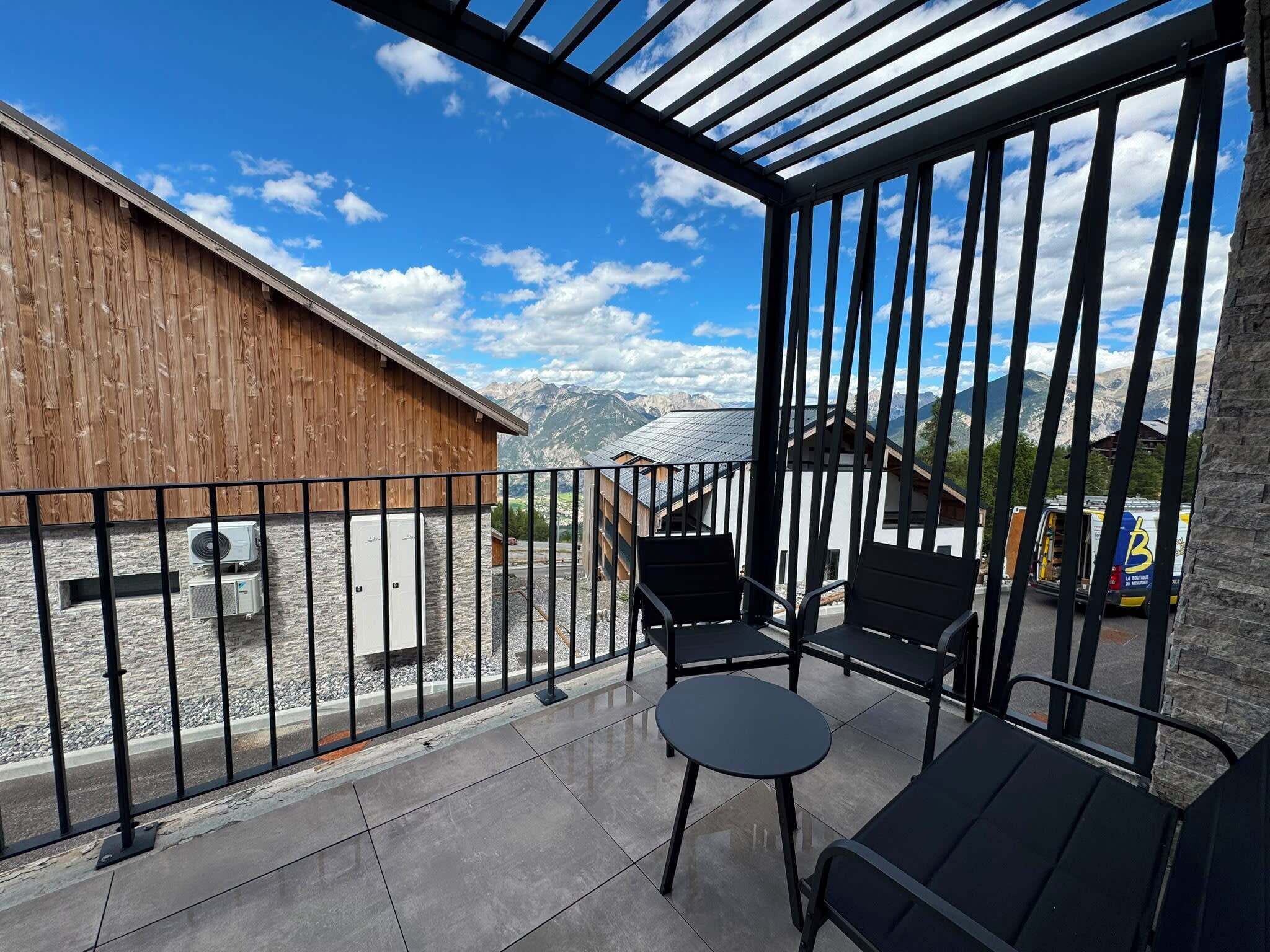 A balcony with a view of mountains, a wooden building, and a parked van.