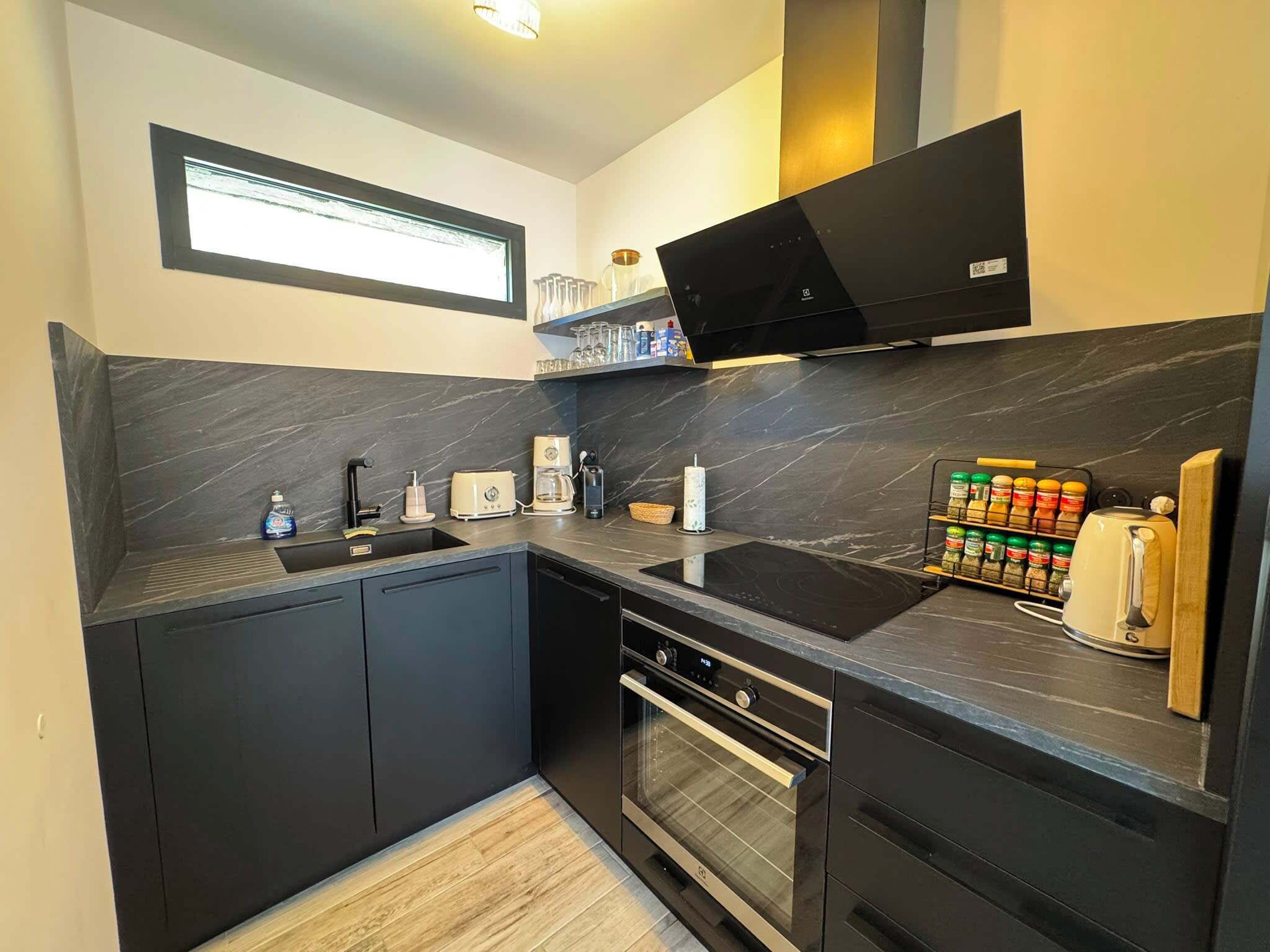 A modern kitchen with dark cabinetry, a built-in oven, a microwave, and a coffee maker.