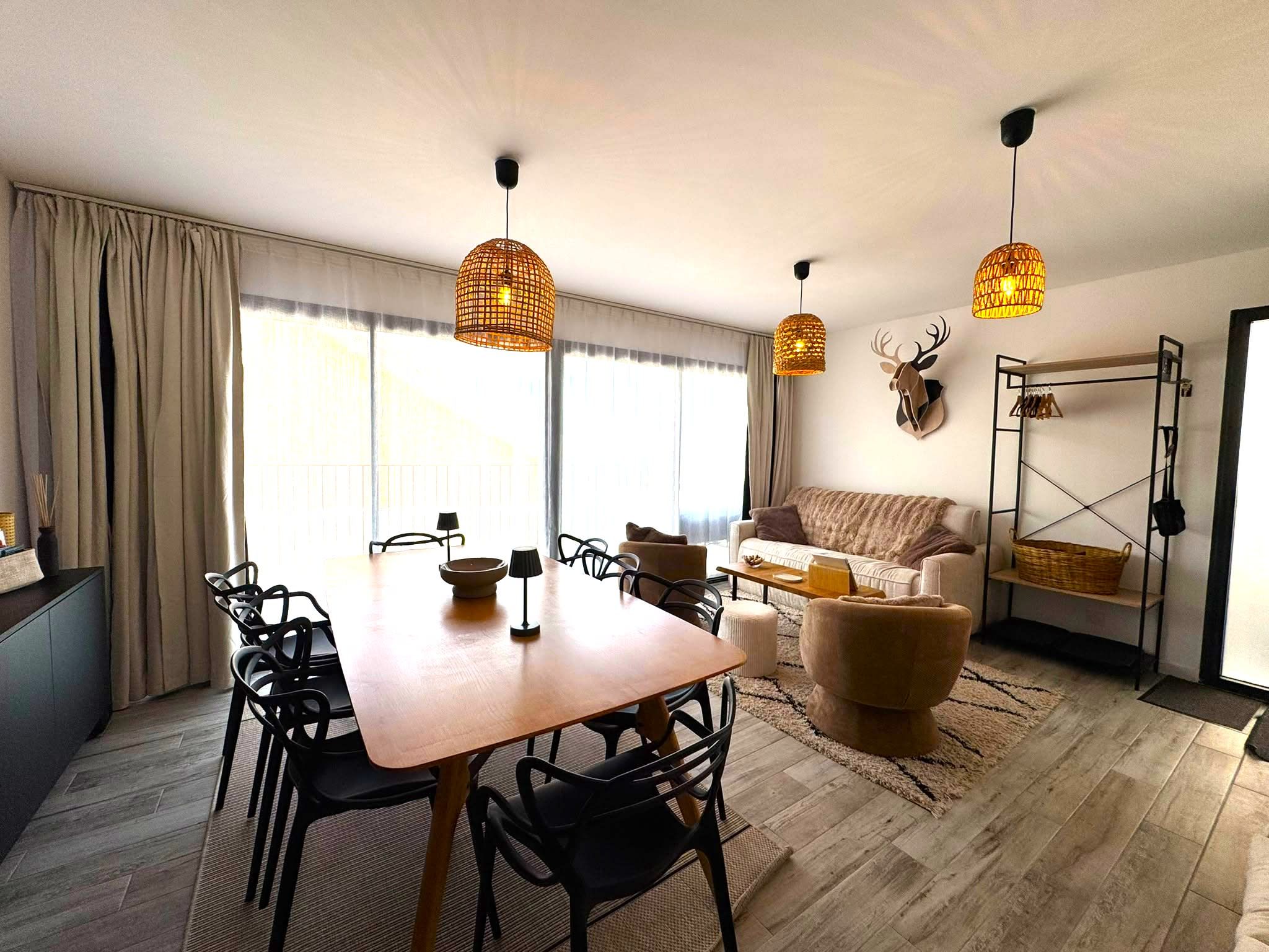 A modern living room with a dining area, featuring a wooden table, black chairs, a sofa, and a decorative wall piece.