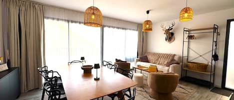 Una sala de estar moderna con comedor, que incluye una mesa de madera, sillas negras, un sofá y un elemento decorativo en la pared.