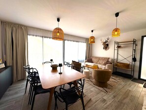 Un soggiorno moderno con zona pranzo, caratterizzato da un tavolo in legno, sedie nere, un divano e un elemento decorativo a parete.