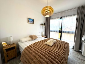 A bedroom with a large bed, a bedside table with a lamp, a hanging plant, and a window with curtains. - Chalet Élégance - 8 pers - 3 chambres - 2 salles de bains (Risoul 1850)