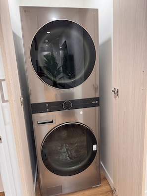 A compact, stainless steel wall-mounted washer and dryer unit with a control panel and a visible reflection of a person and a plant. - Awesome 4-bedroom house with AC in charming Los Angeles (Los Angeles)