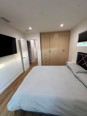 Ein Schlafzimmer mit einem Bett, einem Kleiderschrank, einem an der Wand befestigten Fernseher und einem Fenster mit Jalousien.