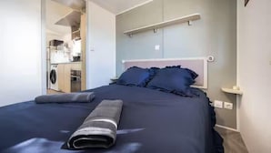 Una camera da letto con un letto, un comodino, una mensola a parete e vista sull'area cucina.
