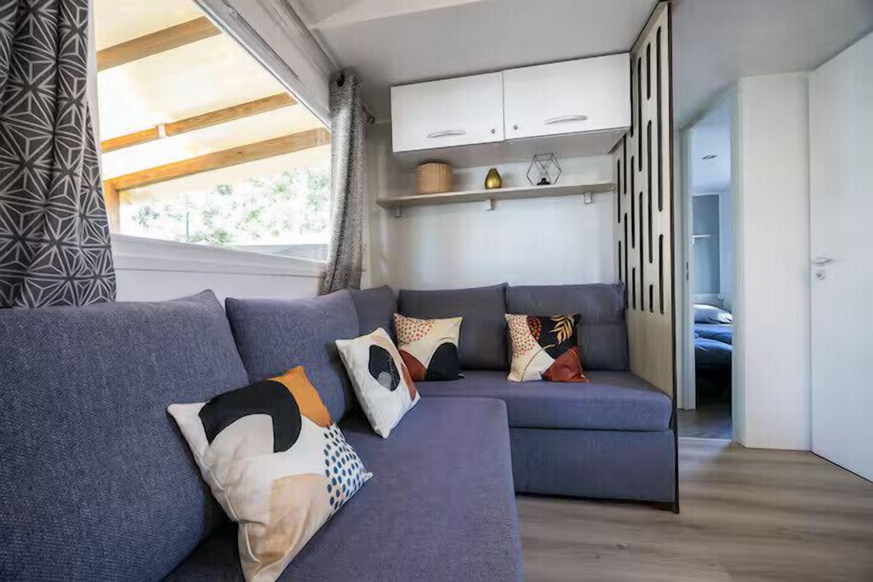 A modern living room with a sectional sofa, a built-in cabinet, and a view of the outdoors.