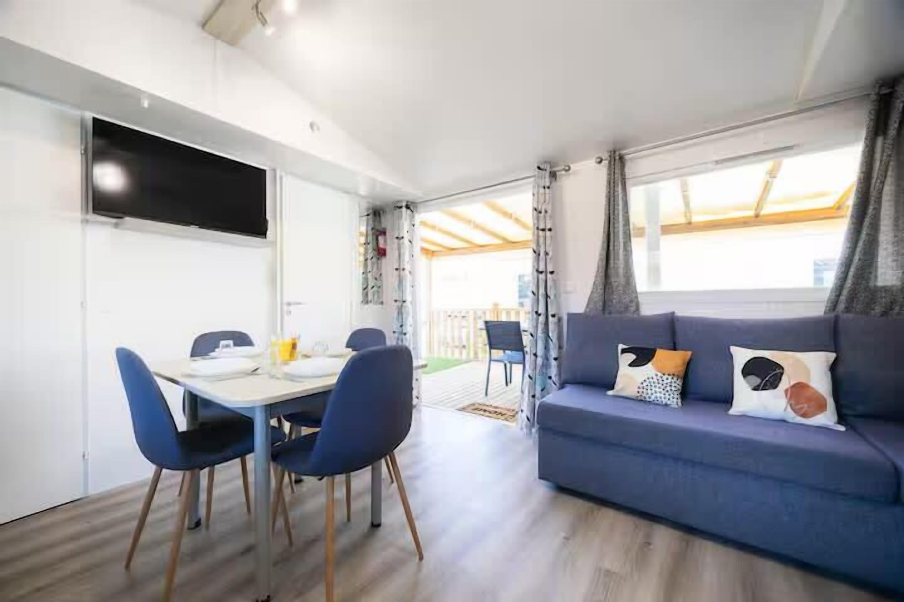En moderne stue med sofa, spisebord med stole og et tv ophængt på væggen.