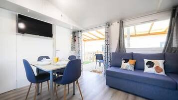 En moderne stue med sofa, spisebord med stole og et tv ophængt på væggen.