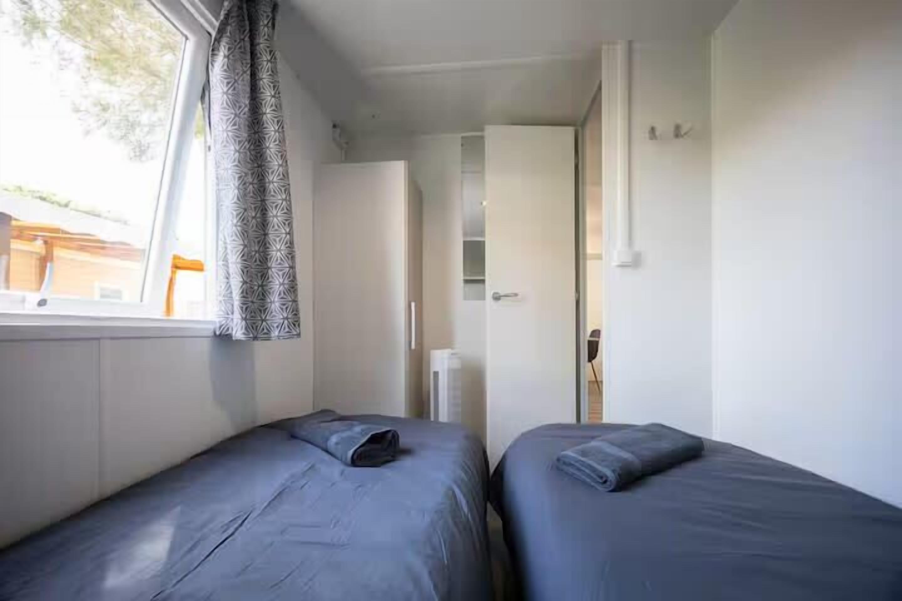 A room with two beds, a window with curtains, a door, and a white wall.