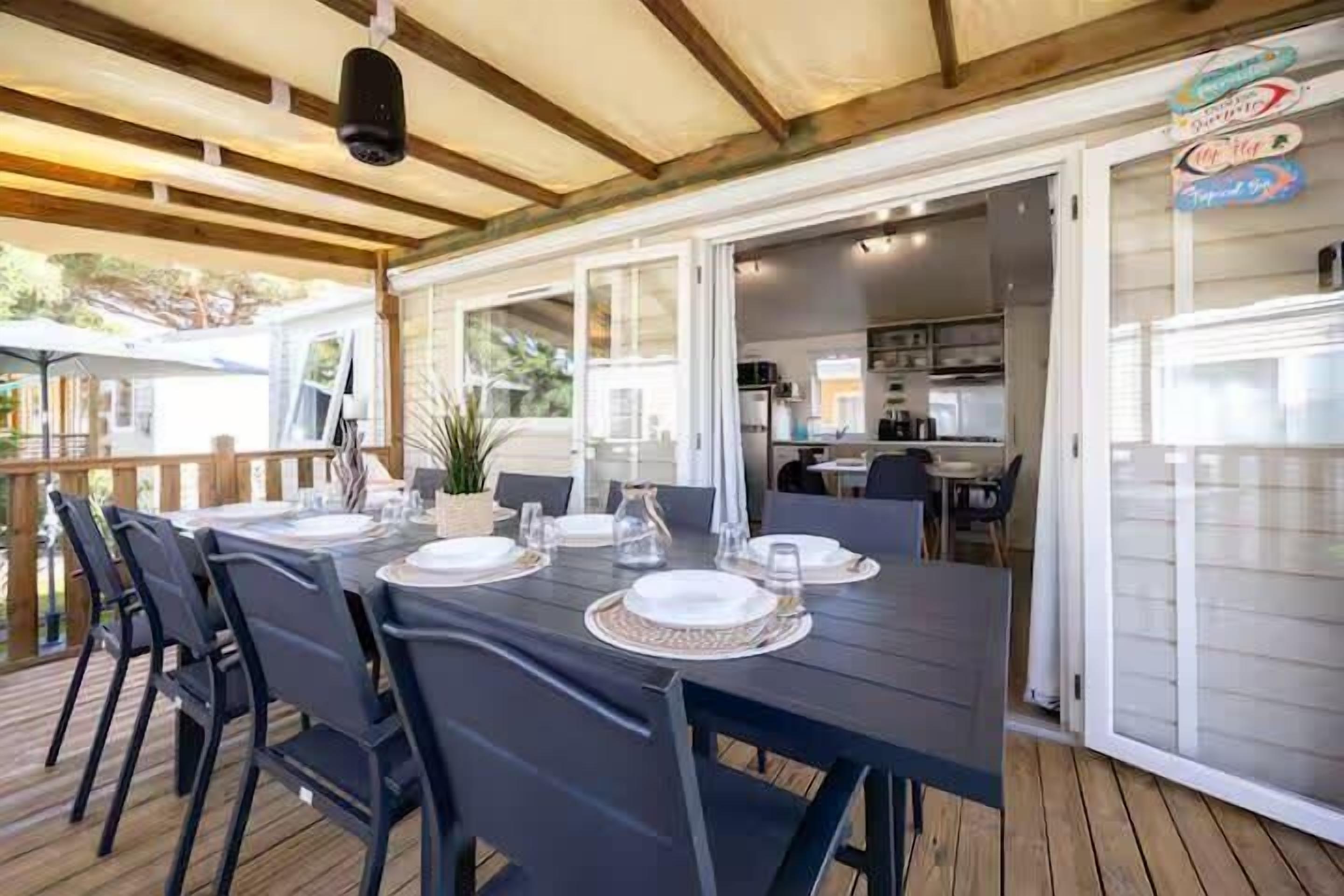 An outdoor dining area with a table set for four, surrounded by chairs, and a view of the kitchen in the background.