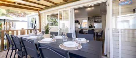 An outdoor dining area with a table set for four, surrounded by chairs, and a view of the kitchen in the background.