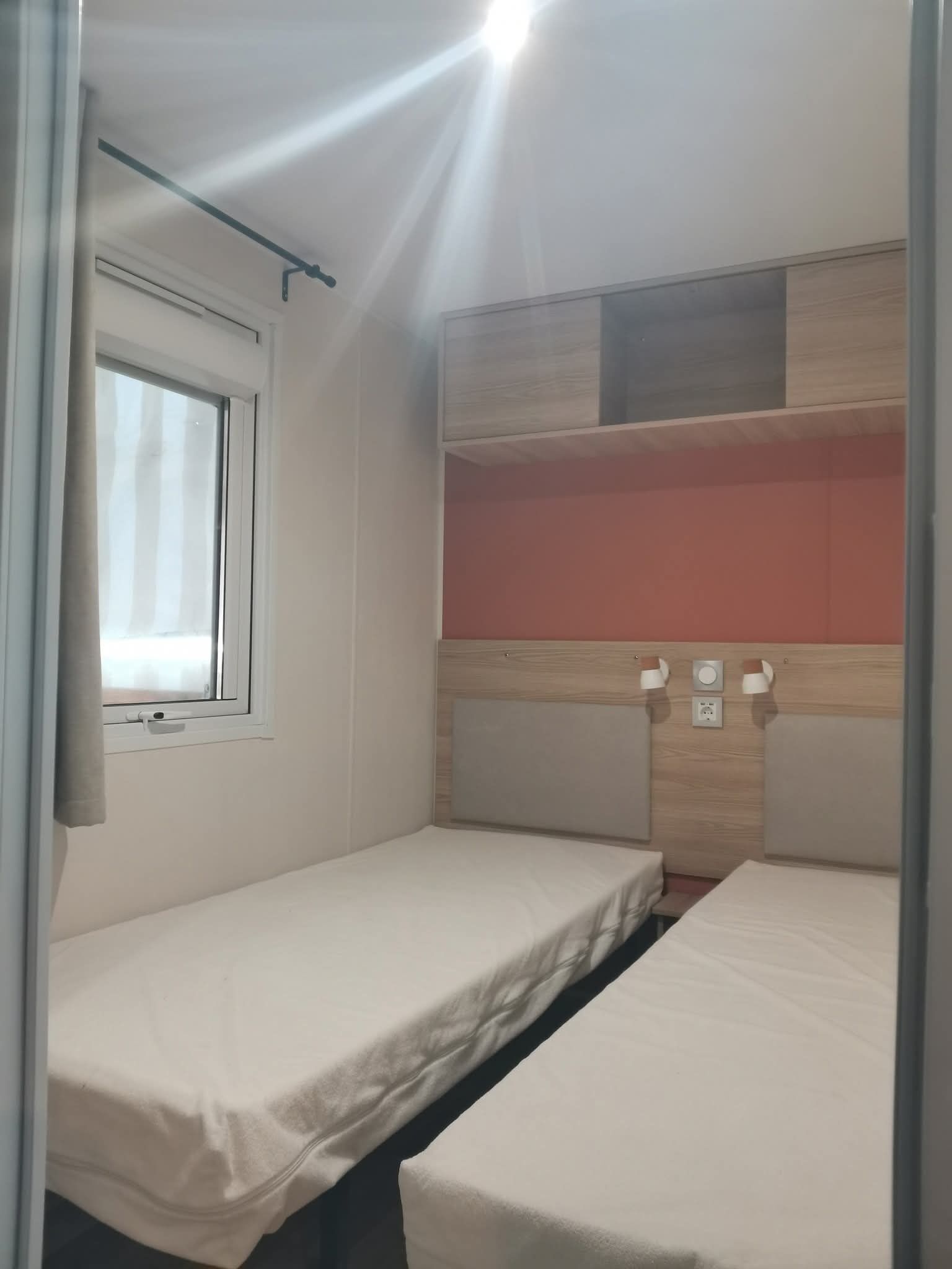 Un petit logement composé d’une seule pièce, avec deux lits, une fenêtre et une étagère intégrée.