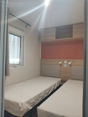 A small, single-room accommodation with two beds, a window, and a built-in shelf. - Mobilhome 2 chambres 6 personnes (Saint-Thomas-de-Conac)