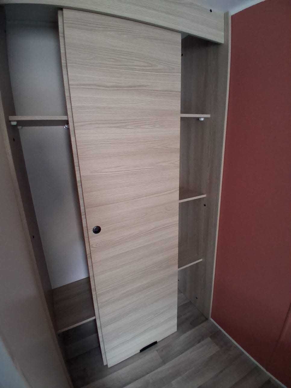 A wooden wardrobe with multiple shelves and a door.