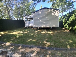 A small, single-story shed with a sloped roof, situated in a grassy backyard with a paved edge. - Mobilhome 2 chambres 6 personnes (Saint-Thomas-de-Conac)