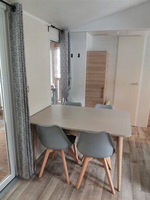 A dining area with a table and chairs, a wooden door, and a patterned curtain. - Mobilhome 2 chambres 6 personnes (Saint-Thomas-de-Conac)