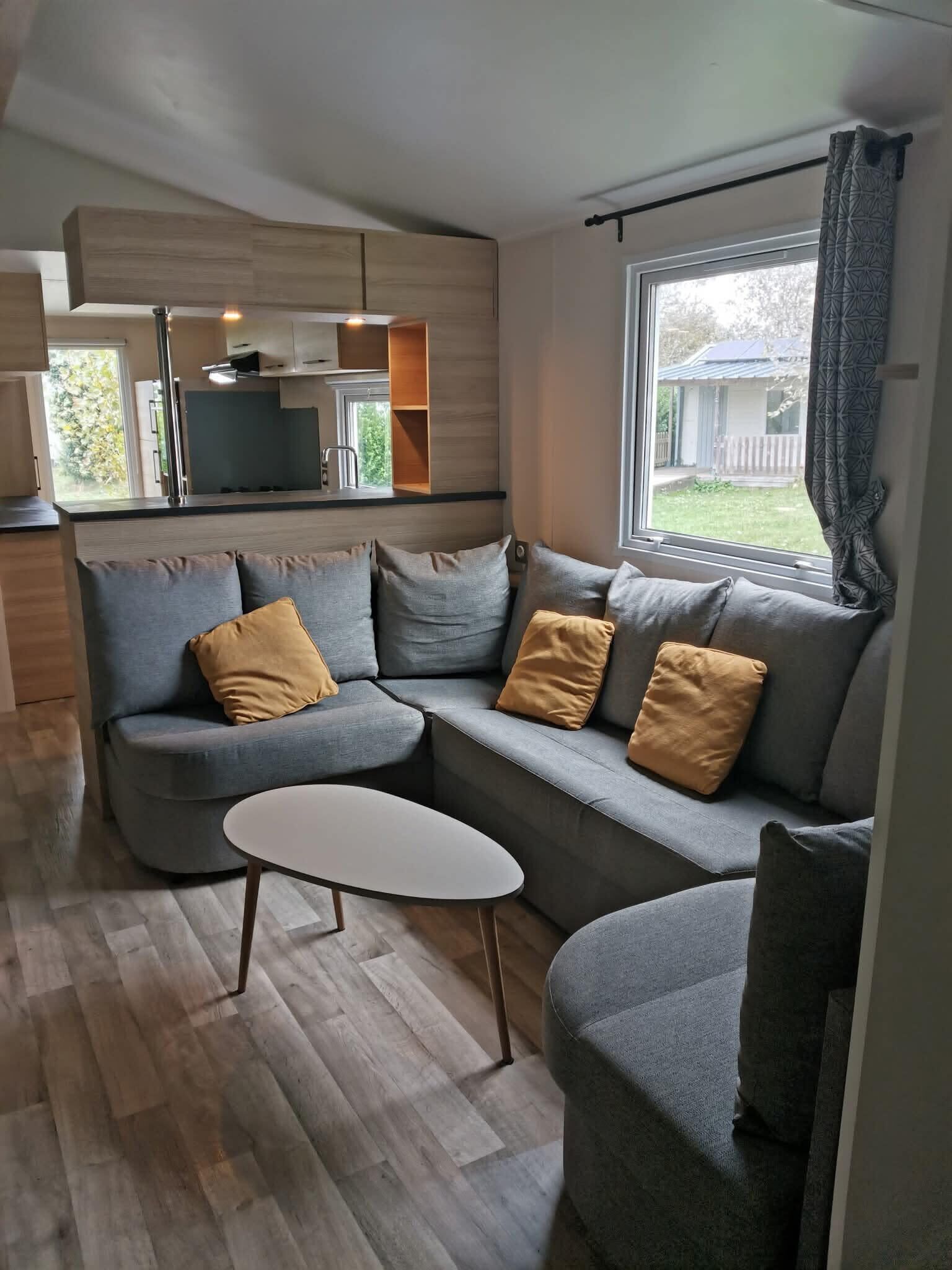 Ein modernes Wohnzimmer mit einem grauen Sofa, einem weißen Couchtisch und Blick ins Freie.