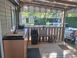 Un espace cuisine extérieur abrité, équipé d’un évier, d’une table en bois et d’un banc.