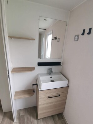 A bathroom with a white sink, a mirror, and wooden shelves. - Mobilhome 2 chambres 6 personnes (Saint-Thomas-de-Conac)