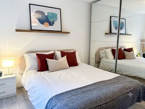 A hotel room with a large bed, a bedside table, a lamp, and a mirror. - Charming 1 bedroom flat in London Excel Docklands (London)