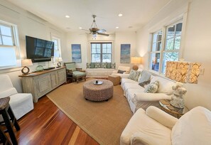 A well-lit living room with a television, seating area, and a ceiling fan. - Luxury Old Seagrove Retreat, Walk to Beach and Seaside, 3 King BRs, Private Heated Pool (Seagrove Beach)