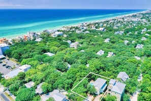 Vista aerea di una zona residenziale con case immerse nel verde, una spiaggia e l'oceano sullo sfondo.