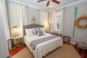 A neatly arranged bedroom with a bed, bedside lamps, a small table, and a window with curtains. - Luxury Old Seagrove Retreat, Walk to Beach and Seaside, 3 King BRs, Private Heated Pool (Seagrove Beach)