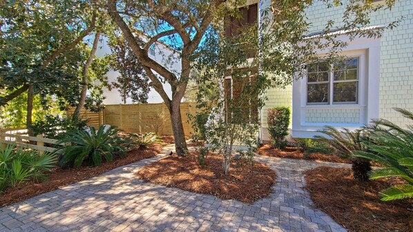 A paved pathway leading to a house with a wooden fence and various plants. - Luxury Old Seagrove Retreat, Walk to Beach and Seaside, 3 King BRs, Private Heated Pool (Seagrove Beach)