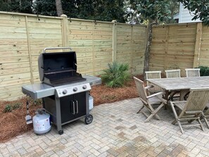 Una griglia da barbecue all'aperto, con bombola del gas, un tavolo con sedie e un recinto di legno sullo sfondo.