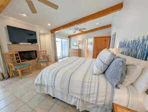 Ein Schlafzimmer mit einem großen Bett, einem an der Wand montierten Fernseher über einem Kamin und einem Deckenventilator.