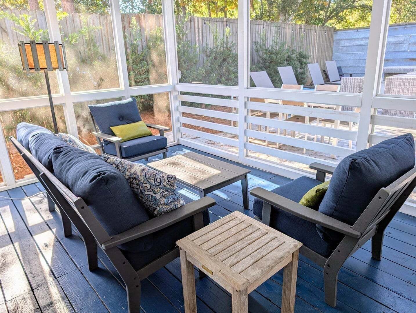Zona salotto esterna coperta, con mobili in legno e recinzione bianca.