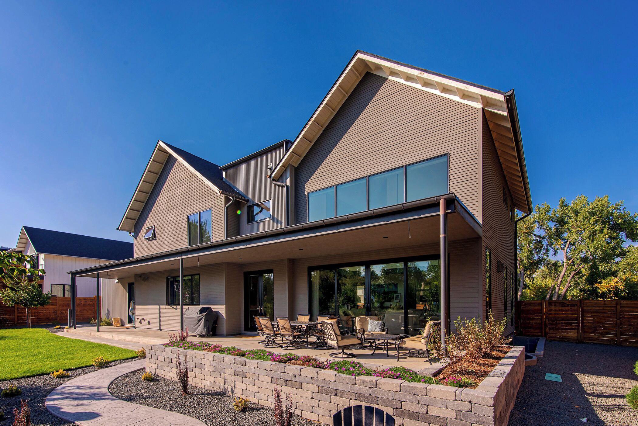 A modern two-story house with a covered patio area, large windows, and a well-maintained lawn.