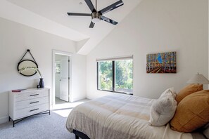 Een slaapkamer met een bed, een dressoir, een plafondventilator, een raam en een schilderij.