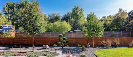 A landscaped backyard with a wooden fence, a variety of plants, and a lawn.