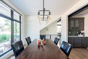 Een eethoek met een houten tafel, zwarte stoelen en een kroonluchter. Er is uitzicht op een balkon met planten en een stoel.
