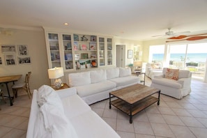 A spacious living room with a white sofa, a coffee table, and a bookshelf filled with various items. - Yellow House, Gulf Front, Private Steps to Beach (Seagrove Beach)