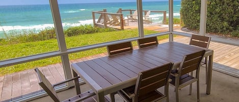 A wooden table with chairs on a balcony overlooking the ocean.