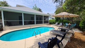Ein Schwimmbecken mit überdachter Terrasse, Liegestühlen und einem Tisch mit Sonnenschirm.