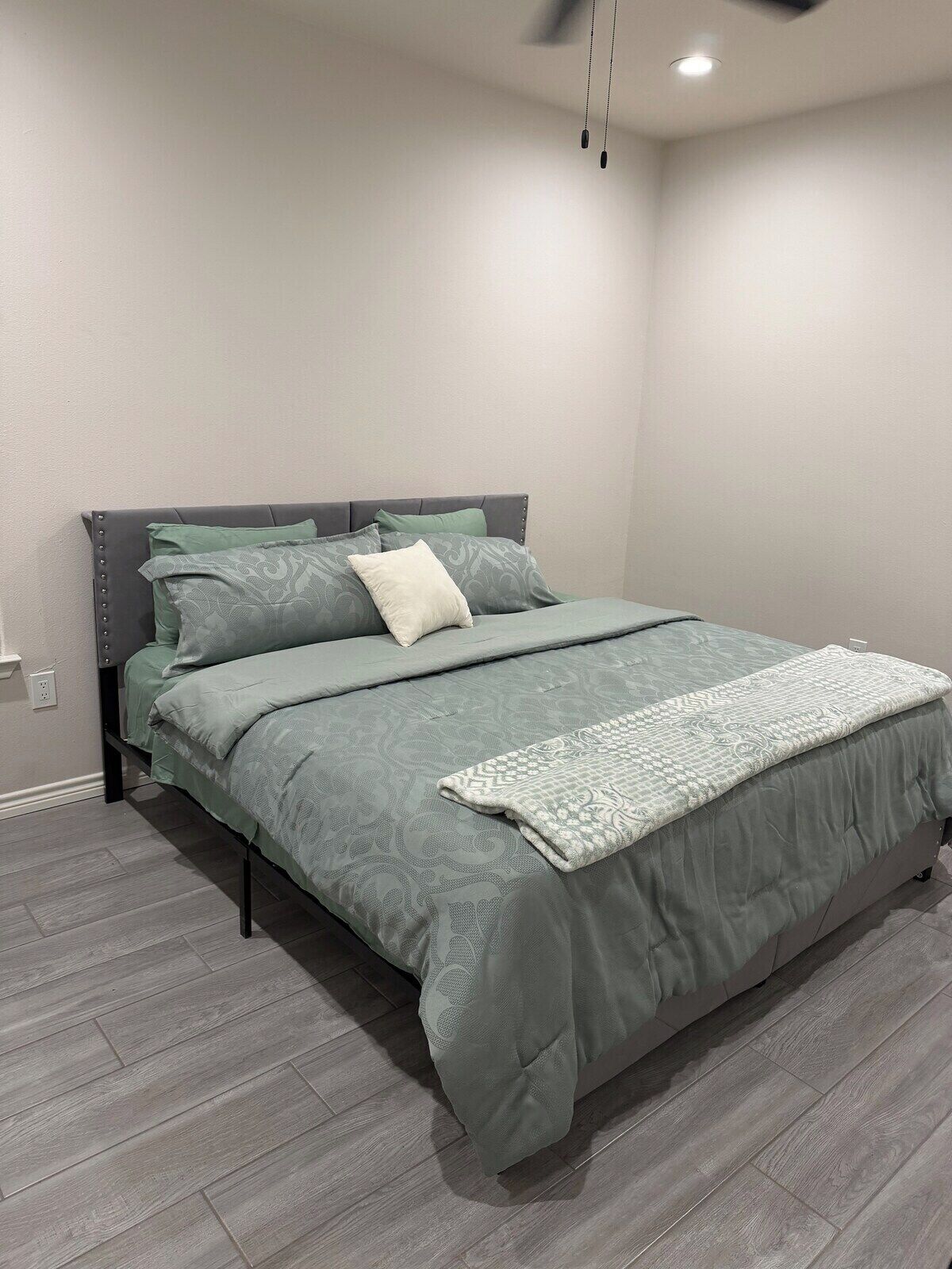 Quarto moderno com cama, roupa de cama cinza e piso cinza.